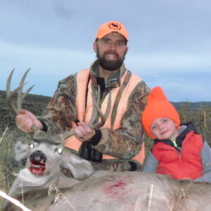 A man and a child, both wearing florescent orange, pose with a recently aharvested mule deer buck.